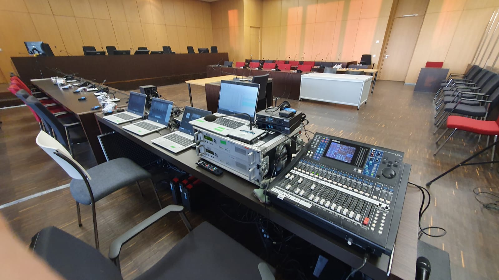 Technische Ausrüstung im Gerichtssaal, einschließlich Laptop, Mikrofonen und Audiotechnik, zur Unterstützung der Simultanübersetzung und Videostreaming in einer Gerichtsverhandlung.